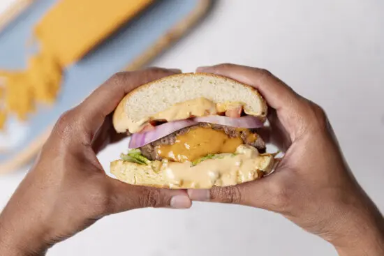 Two hands holding a stuffed cheddar burger with a block of cheese in the background